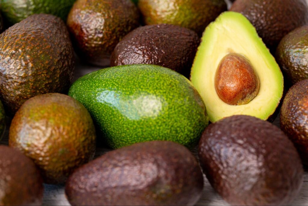 a cut avocado fruit next to other ripe ones